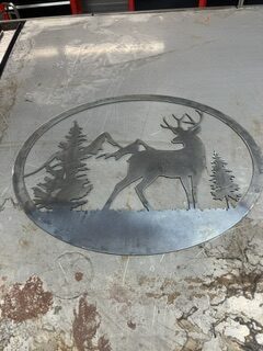 Custom plasma-cut metal deer and forest scene displayed on a workshop table